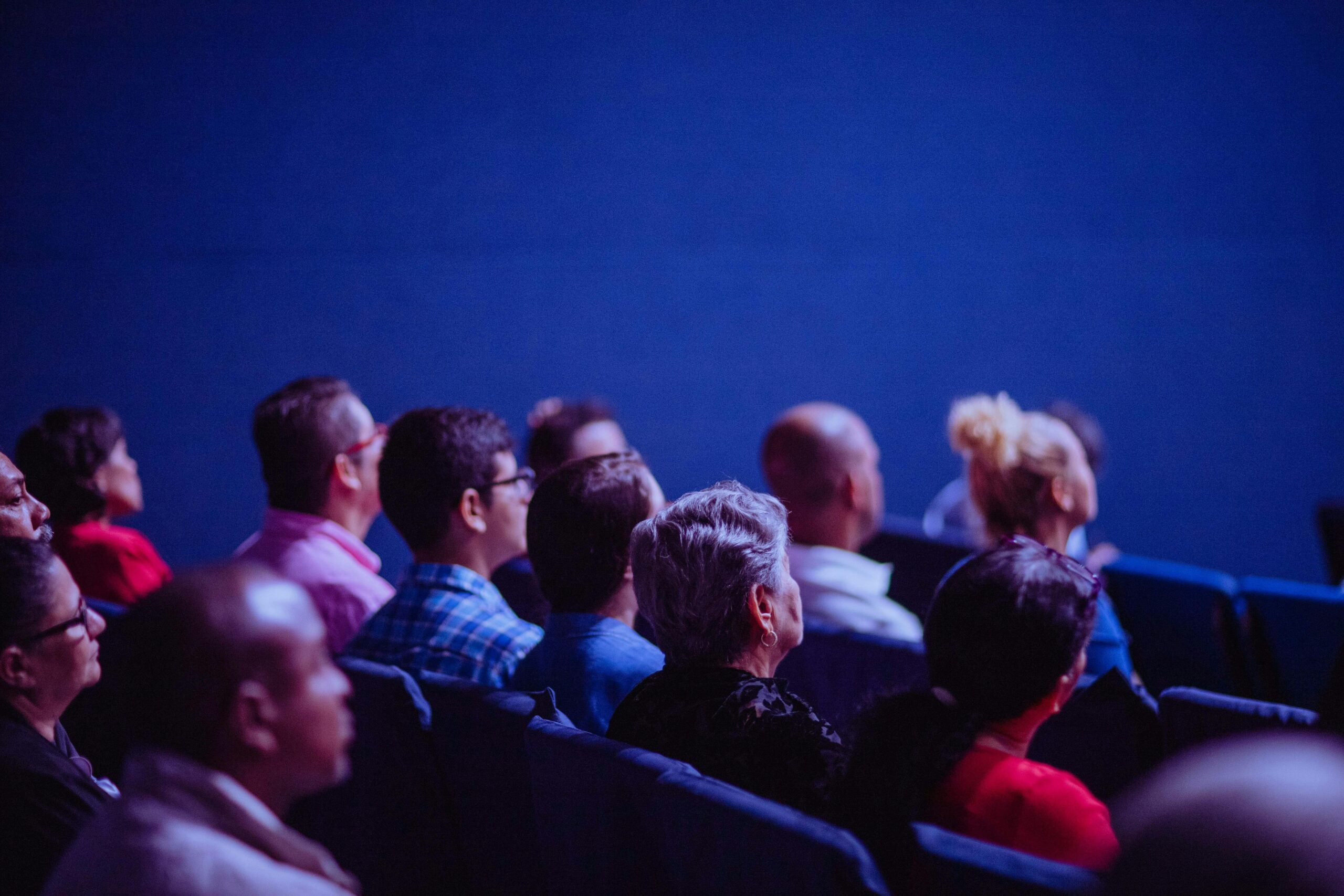 An attentive group of adults seated at an indoor conference, focusing on a presentation.